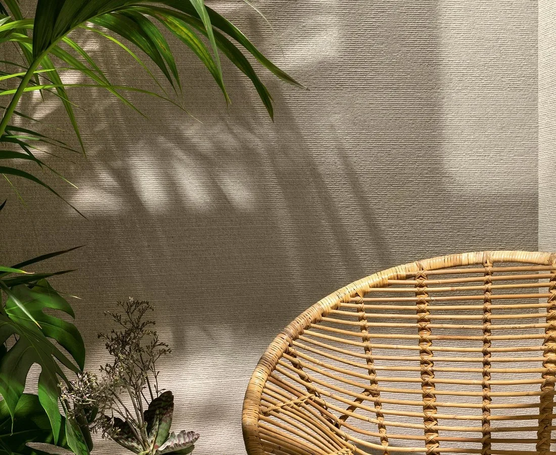 Parete materica in gres con poltrona in rattan e luce naturale